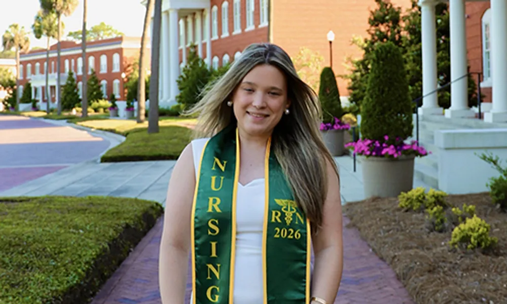 Photograph of a young woman wearing a green and gold nursing graduation stole with 