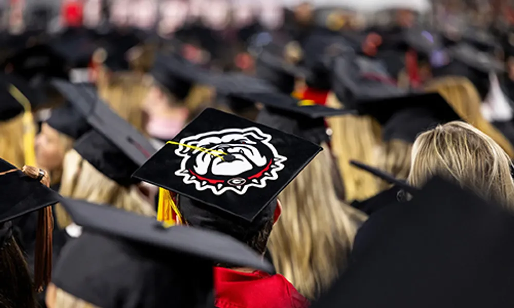 A mortarboard decorated with the Georgia Bulldog logo stands out among rows of graduates and mortarboards at Commencement.