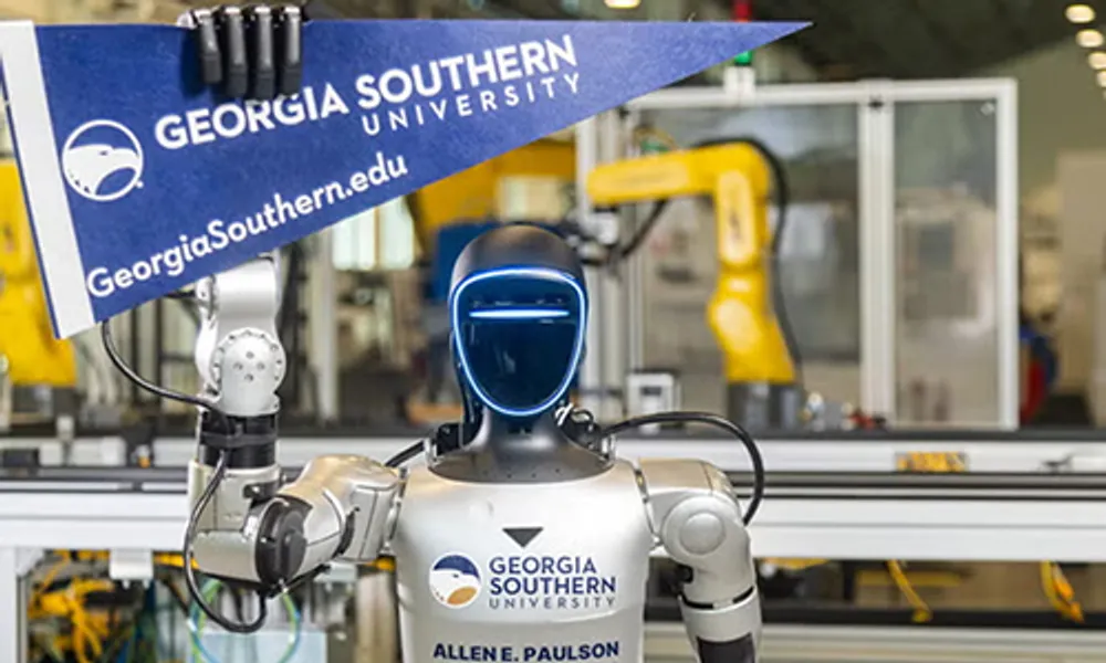 Photograph of a humanoid robot holding a Georgia Southern University pennant in a robotics lab. Robot features a sleek black face with blue LED lights, metallic arms, and a torso labeled with university and college of engineering logos, with industrial robotic arms visible in the background.