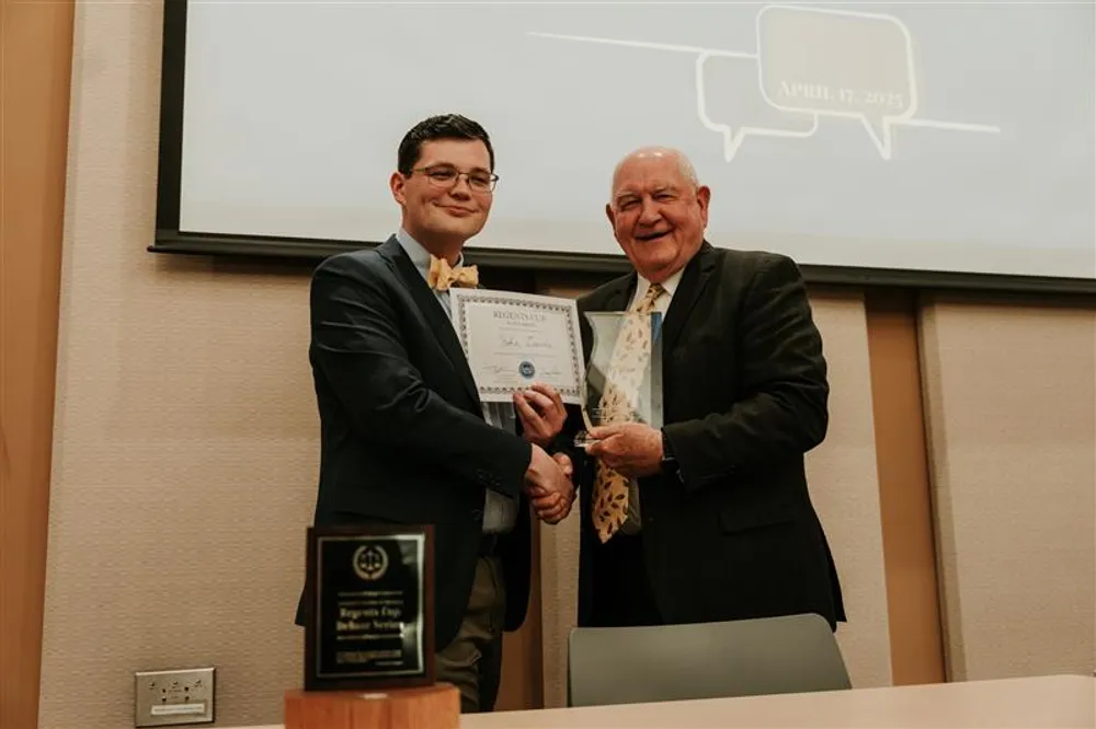 Chancellor Sonny Perdue presents a trophy to individual debater John Davis at the tournament in 2025