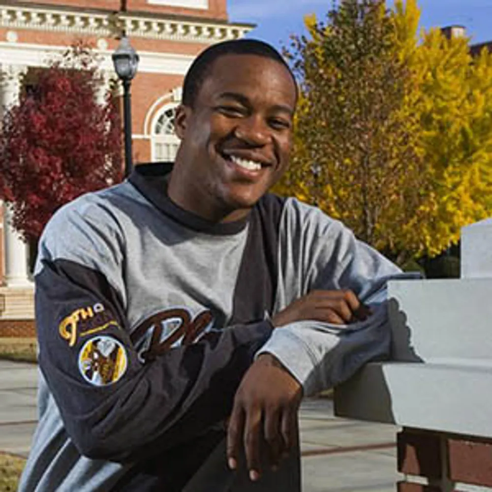 A smiling student leaning on a building column with his elbow looking at the camera