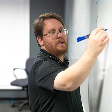 Teacher writing on a a dry erase board with a blue marker.
