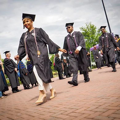 Students at graduation walking on a red brick pathway.  They are dressed in black graduation gowns.