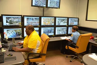 Control room with two men looking at array of screens